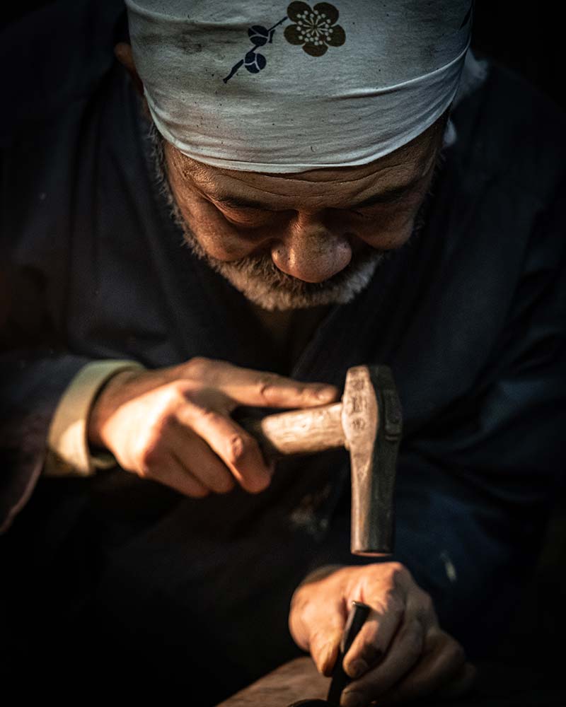 The blacksmith is hard at work hammering an etching into a freshly made knife in Kochi Japan