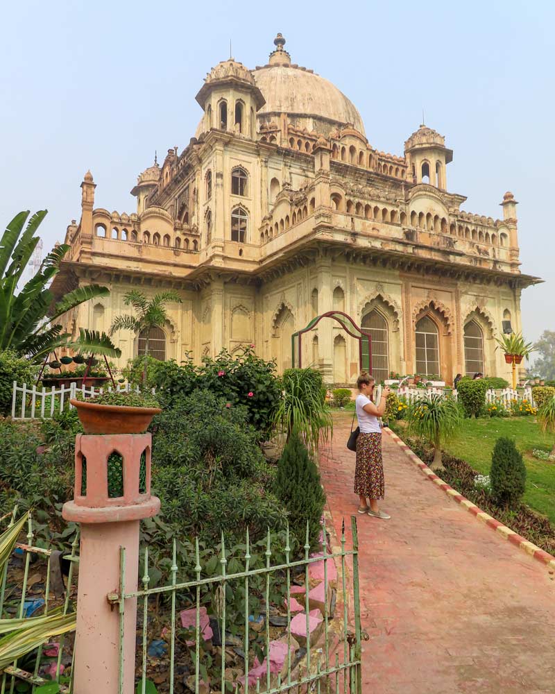 A lady stands infront of an old building in Lucknow Delhi surrounded by verdant gardens