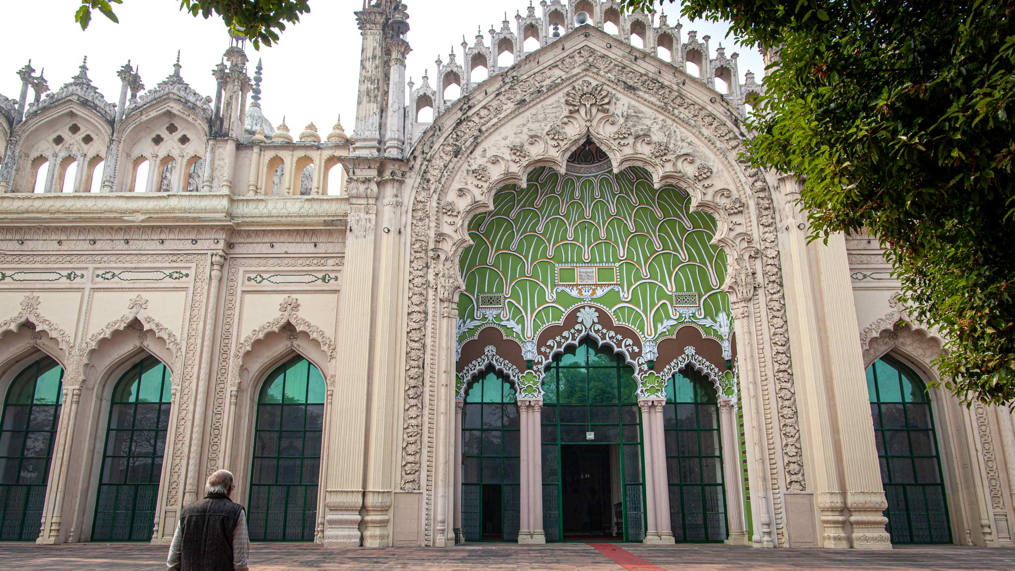 The entrance gate to Jama Masjid Mosque in Lucknow, where a man stands praying to the left and various archways with colourful tiles are on the building