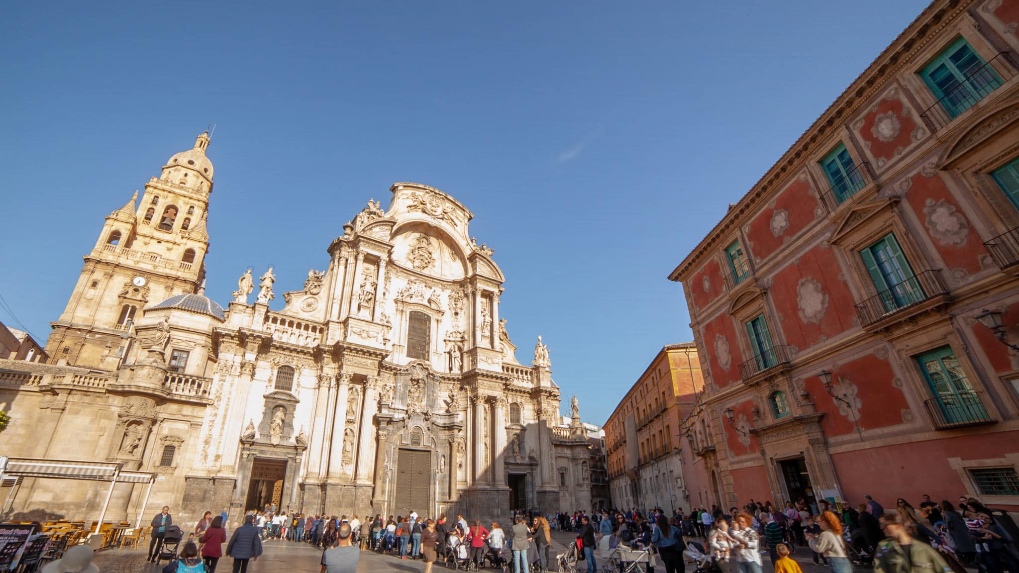 The main square in Murcia with a cathedral on the left and a red fronted palace on the right