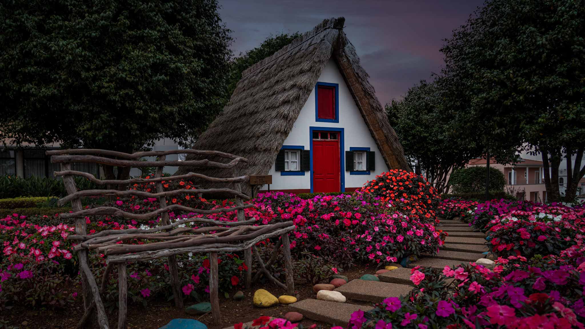 The traditional thatched houses of Santana, a pointed triangle shaped house with colourful blue and red windows and flowers outside