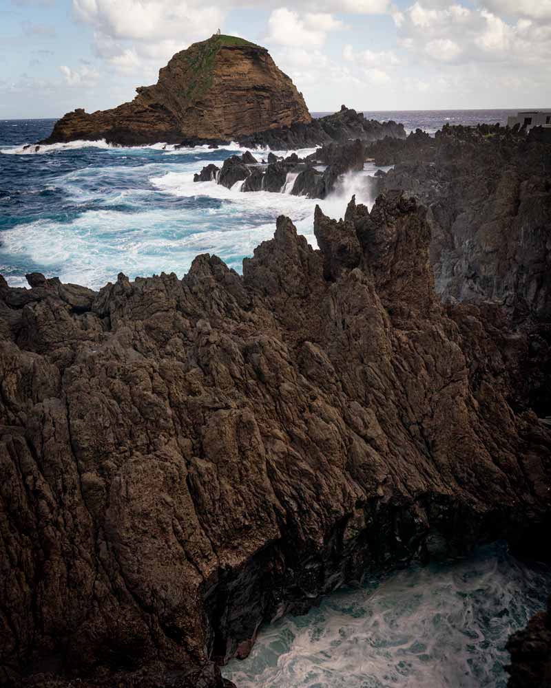 Dramatic rock formations around Porto Moniz with waves crashing against them and sending spray flying