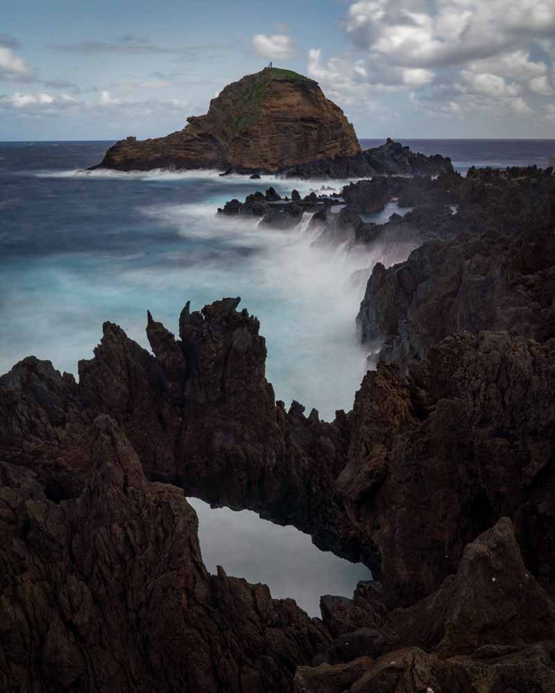 Dramatic rock formations around Porto Moniz with waves crashing against them and sending spray flying